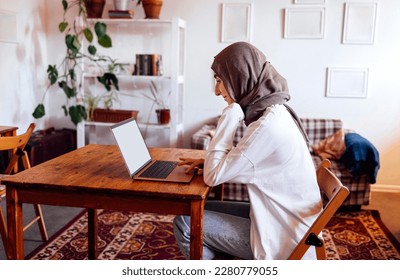 Pretty young middle eastern woman wearing hijab using laptop at home. Muslim girl preparing for entry exams. Home education and online studing concept - Shutterstock ID 2280779055