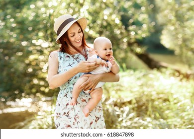 Pretty Young Mother In Hat Holding Newborn Baby Boy, Sunny Summer Spring Nature Background