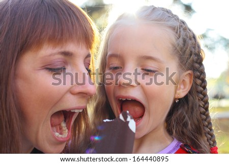 pretty young mother and her cute little daughter eating ice cream together in the park