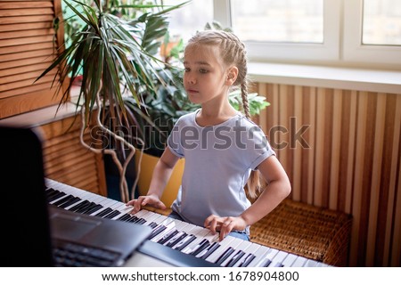 Pretty young musician playing classic digital piano at home during online class at home, social distance during quarantine, self-isolation, online education concept