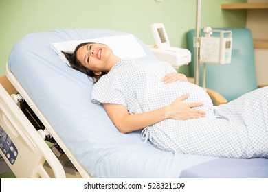 Pretty young pregnant woman getting labor contractions while lying on a hospital bed - Powered by Shutterstock