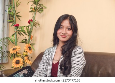 A Pretty Young Professional Looking At The Camera While Sitting At The Couch. Late Teens And Early 20s Woman In Business Attire.