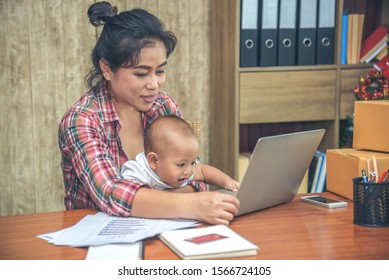 Pretty Young Single Mom Working At Home On A Laptop Computer While Holding Her Baby Girl Sitting On Her Lap Enjoying Playing Computer.