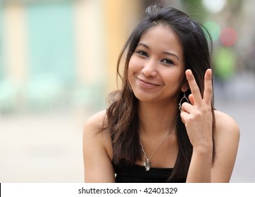 Pretty Young Smiling Asian Woman On The Street Making The Peace Sign