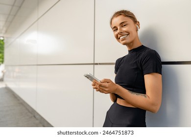 pretty young smiling woman doing sports in the morning in black stylish sport outfit sportswear, skinny strong body, healthy fit lifestyle, posing against the wall using smartphone - Powered by Shutterstock