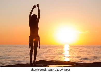 Pretty Young Teen With Long Hair Dancing In Black Bikini Against An Ocean And Sunset . Concept Of Happy Serene Freedom Woman