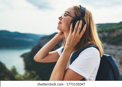 pretty young tourist woman with backpack and  hipster glasses closes her eyes listens favorite music with headphones enjoying freedom of  hiking background natura mountain landscape on trip outdoors - Shutterstock ID 1771131047