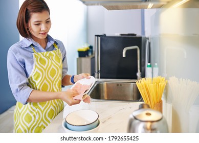 Pretty young Vietnamese housewife wiping plates with soft cloth after finishing cooking