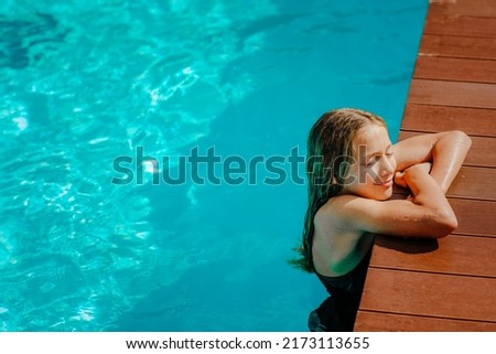 Pretty young wet girl in summer bikini posing in the pool with copy space.