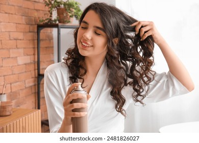 Pretty young woman applying hair spray on her curly hair in bathroom - Powered by Shutterstock