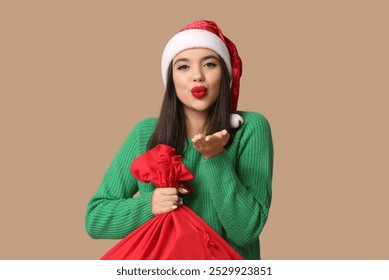 Pretty young woman with bag of Christmas gifts blowing kiss on beige background - Powered by Shutterstock