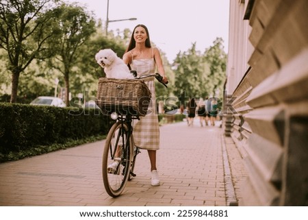 Pretty young woman with a bichon dog in a bicycle basket takes a leisurely ride