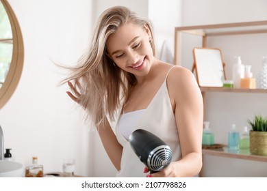 Pretty young woman blow drying her hair in bathroom