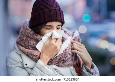 Pretty young woman blowing her nose with a tissue outdoor in winter. Young woman getting sick with flu in a winter day. Woman with a cold.