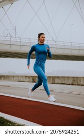 Pretty Young Woman In Blue Track Suit Running By The River At Autumn Morning