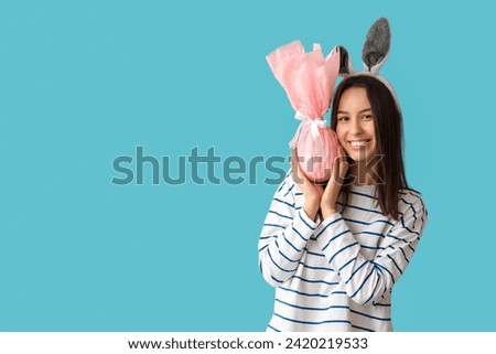 Pretty young woman with bunny ears and Easter gift on blue background
