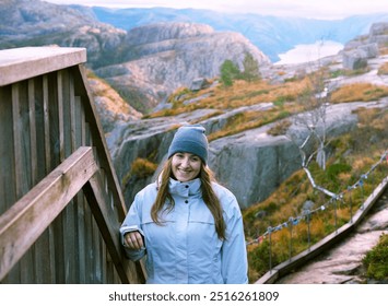 Pretty young woman in cap and coat, smiling on the stairs on the way to the pulpit rock. Winter holiday in Norway. - Powered by Shutterstock