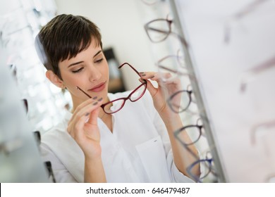 Pretty young woman is choosing new glasses at optics store - Powered by Shutterstock