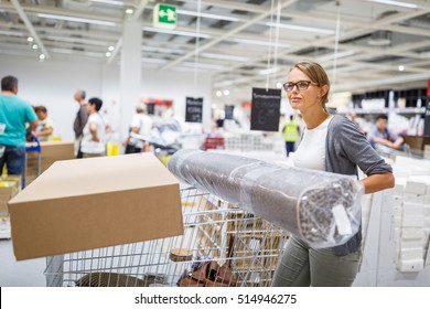 Pretty, Young Woman Choosing The Right Furniture For Her Apartment In A Modern Home Furnishings Store - With A Trolley, Done Shopping, Leaving The Store, Going Home With The Purchased Goods