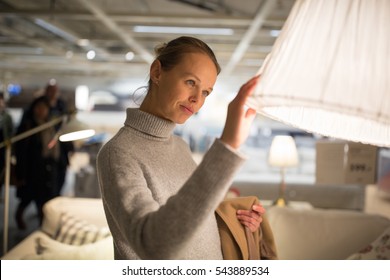Pretty, young woman choosing the right lamp for her apartment in modern furniture