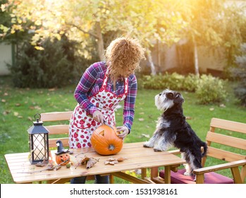 Pretty young woman cutting pumpkin for Halloween in garden while dog making her company