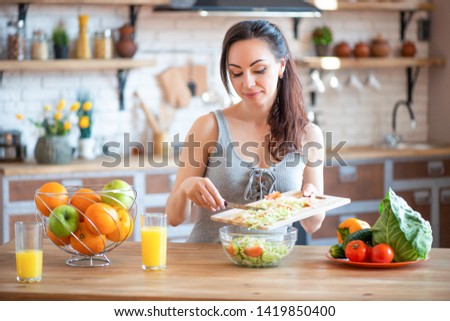 Pretty young woman cutting vegetables salad in the kitchen