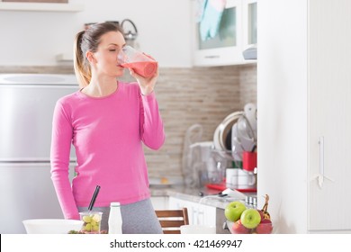 Pretty young woman drinking a fruit smoothie in her kitchen. - Powered by Shutterstock