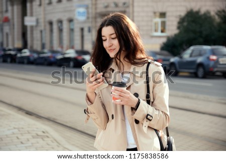 Pretty young woman drinking takeout coffee cup, using smart phone while waiting train as arrival.