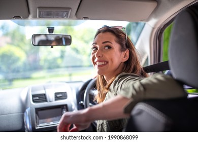Pretty young woman driving car smiling. Attractive woman going in reverse looking back over shoulder. 