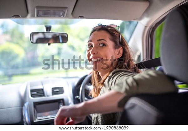 Pretty young woman driving\
car smiling. Attractive woman going in reverse looking back over\
shoulder. 