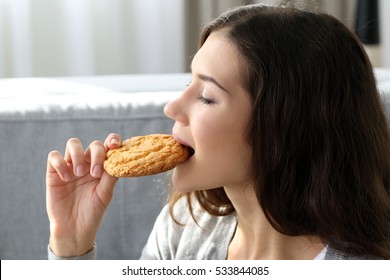 Pretty young woman eating tasty cookie at home, close up
