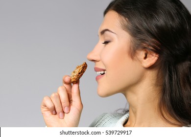 Pretty young woman eating tasty cookie, on grey background