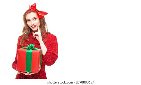 Pretty Young Woman In Elegant Red Dress And Hairbow On Her Head Joyfully Holds A Gift. White Background. Pin-up Style. Copy Space. Holiday Sale Concept.