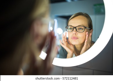 Pretty, Young Woman In Front Of Her Bathroom Mirror In The Morning - Checking Her Face, Getting Ready For Work (color Toned Image; Shallow DOF)