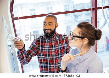 Pretty young woman in glasses and bearded african american man standing near whiteboard and preparing for presentation