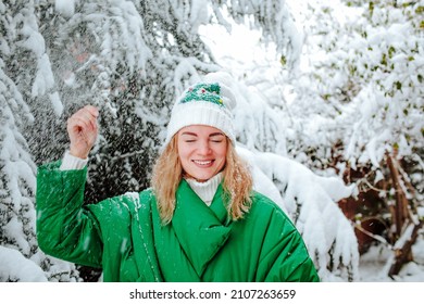 Pretty Young Woman In Green Winter Coat And White Hat Shaking Down Snowing Bronco And Smiling. Winter Concept. 