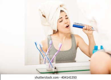 Pretty young woman having fun and singing to a hairbrush after taking a shower