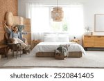 Pretty young woman with headphones listening to music in light bedroom