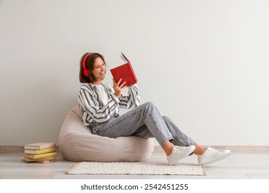 Pretty young woman in headphones reading book on beanbag chair at home - Powered by Shutterstock