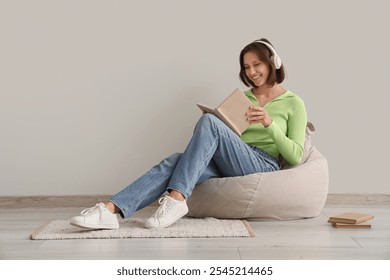 Pretty young woman in headphones reading book on beanbag chair at home - Powered by Shutterstock