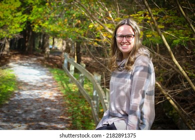 Hübsche junge Frau in ihren 20ern, die in einem Park während der Herbstsaison auf einer Schiene saß und fröhlich lächelte