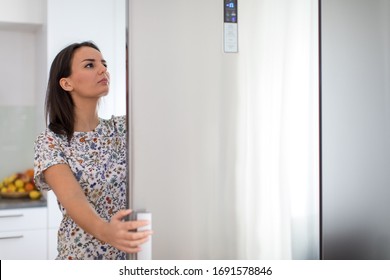 Pretty, young woman in her modern kitchen, by the fridge, about to cook a healthy meel for her family (color toned image)