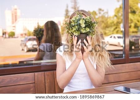 Pretty young woman hide face by green. Outdoors anonymity portrait. Trendy unspecific view. Long blond hair. Unindentified person. Faceless concept