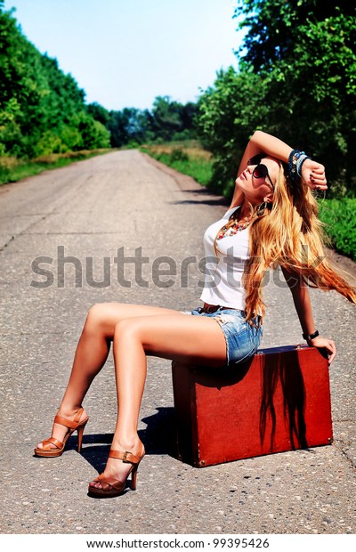 Pretty young woman\
hitchhiking along a\
road.