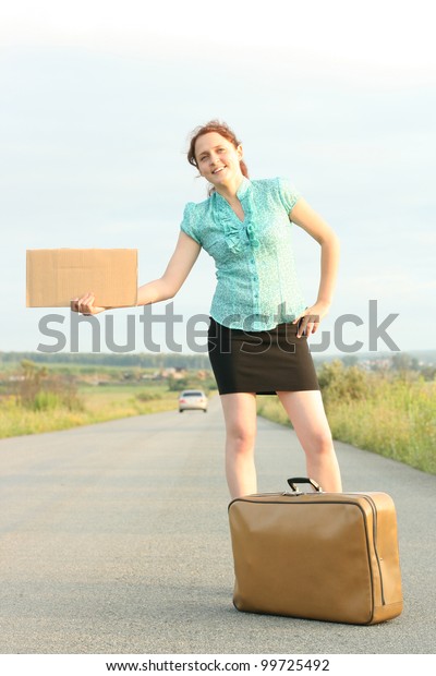 Pretty young woman\
hitchhiking along a\
road.