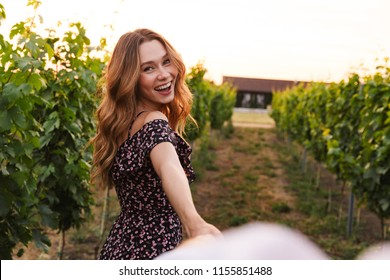 Pretty young woman holding hand of her boyfriend while walking outdoor together through vineyard on summer day. Follow me concept - Powered by Shutterstock