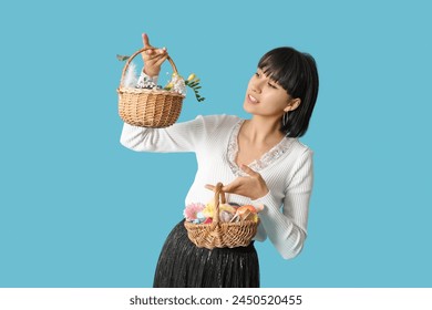 Pretty young woman holding wicker Easter baskets with cosmetics on blue background - Powered by Shutterstock