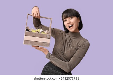 Pretty young woman holding wooden Easter basket with cosmetics on lilac background - Powered by Shutterstock