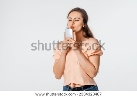 Pretty young woman kissing her mobile phone, standing against white background with copy space. Enthusiastic young woman holding smartphone, feeling excited winning online lottery bid on cellphone