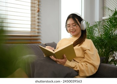 Pretty young woman listening to music with headphone and reading book at home - Powered by Shutterstock